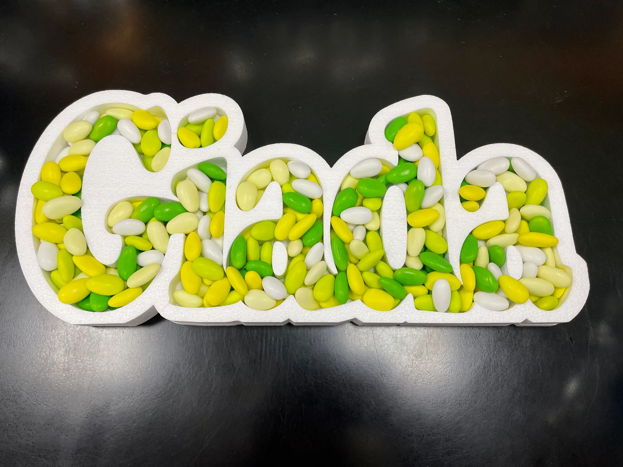 Portaconfetti in polistirolo bianco con il nome Giada scavato e riempito di confetti gialli, verdi e bianchi