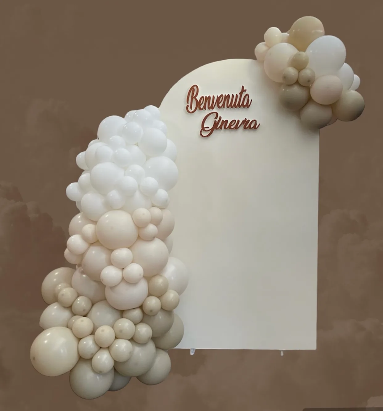 Pannello bianco ad arco con la scritta Benvenuta Ginevra in corsivo marrone e una ghirlanda di palloncini bianchi e beige