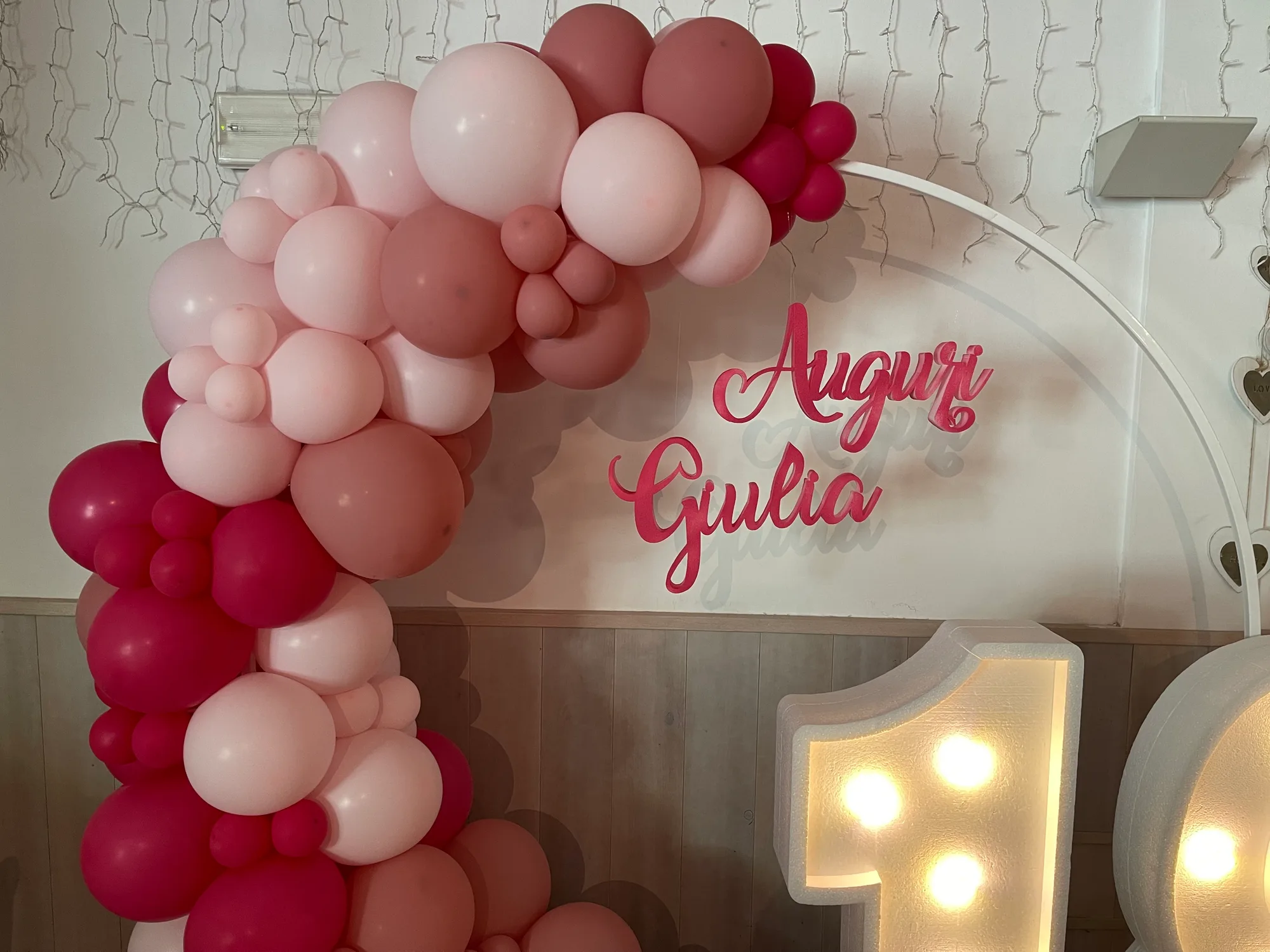 Scritta Auguri Giulia in corsivo fucsia dentro un cerchio con ghirlanda di palloncini rosa e fucsia, accanto a numeri luminosi