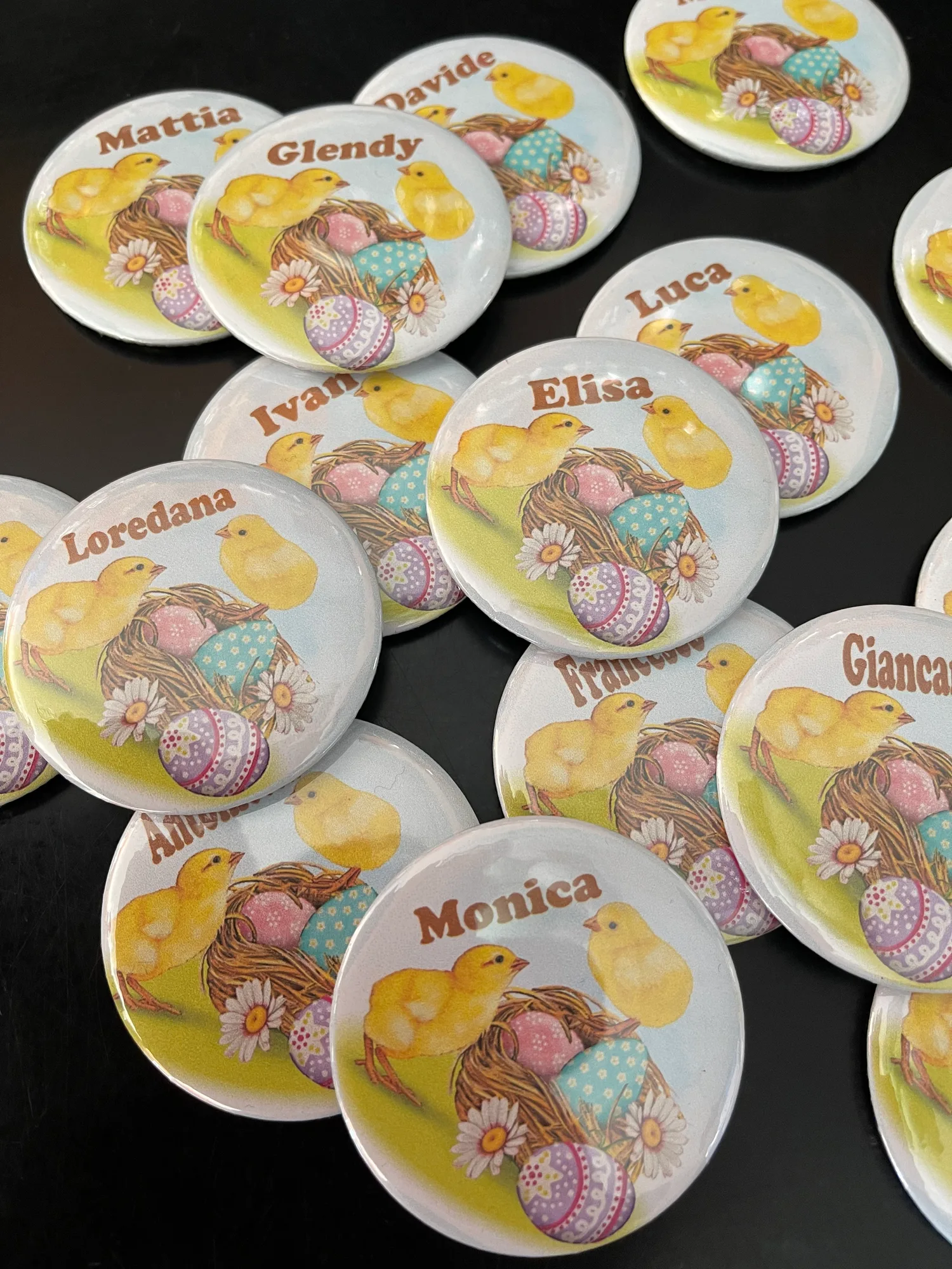 Spille rotonde con pulcini, nido e uova di Pasqua e un nome diverso stampato su ognuna, come Mattia, Elisa e Monica