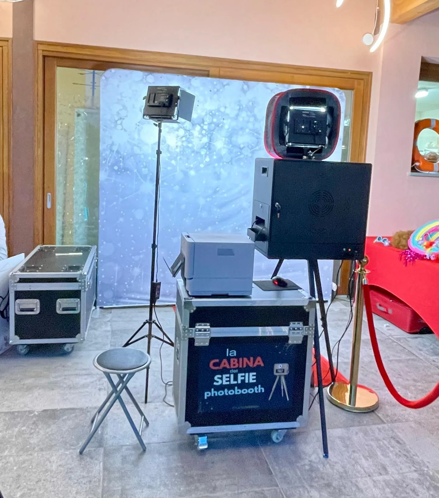 La Cabina del Selfie montata dentro una sala: fondale chiaro, faretto, stampante, sgabello e cordone rosso con colonnina dorata