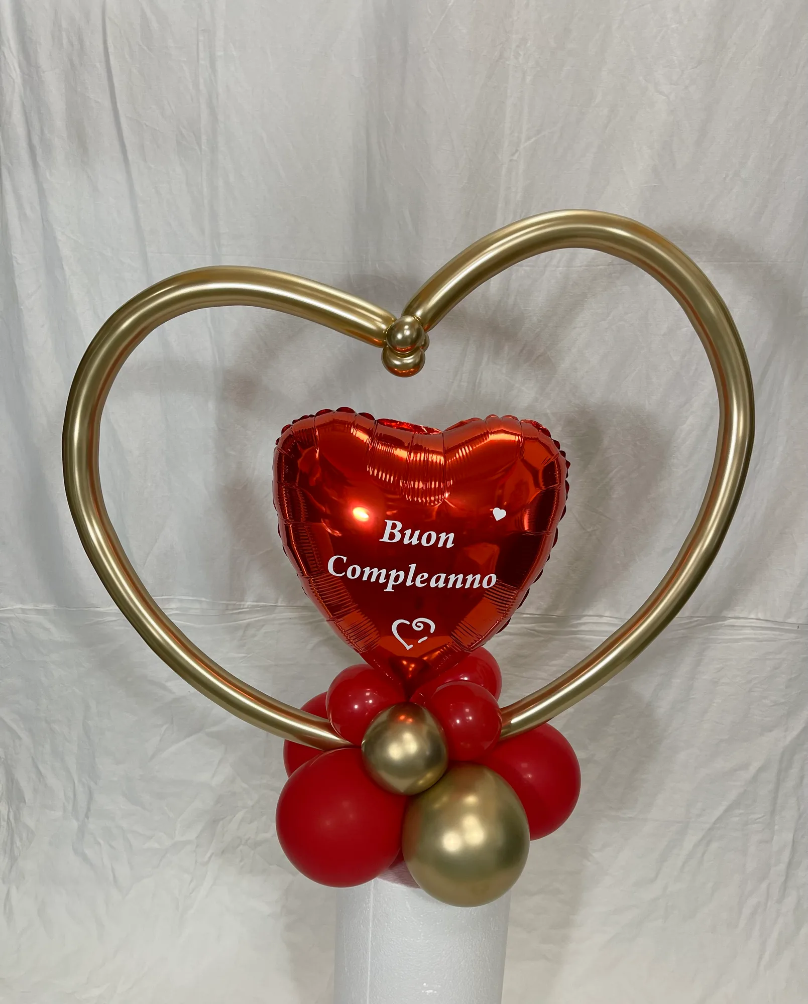 Composizione con un cuore rosso in mylar con la scritta Buon Compleanno, dentro un grande cuore fatto con un palloncino oro, su una base di palloncini rossi e oro