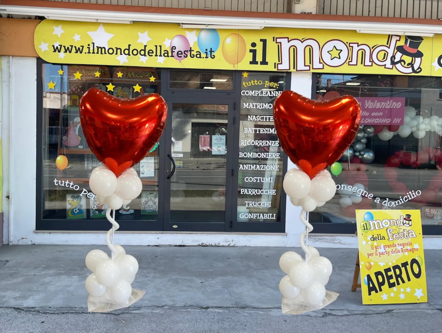 Due colonnine di palloncini bianchi con un grande cuore rosso in mylar davanti alla vetrina del negozio Il Mondo della Festa