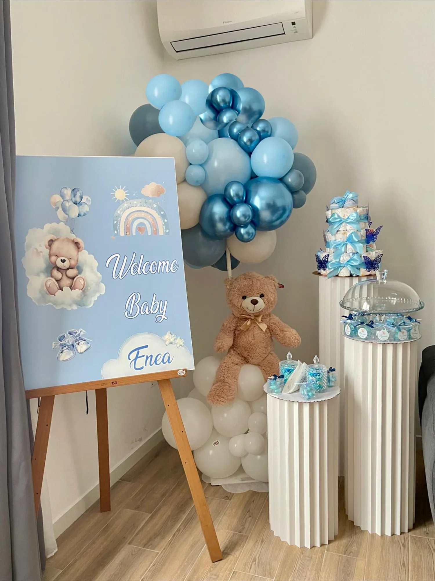Allestimento per il ritorno a casa di Enea: tabellone Welcome Baby su cavalletto, ghirlanda di palloncini celesti e cromati, torta di pannolini e colonne con la confettata