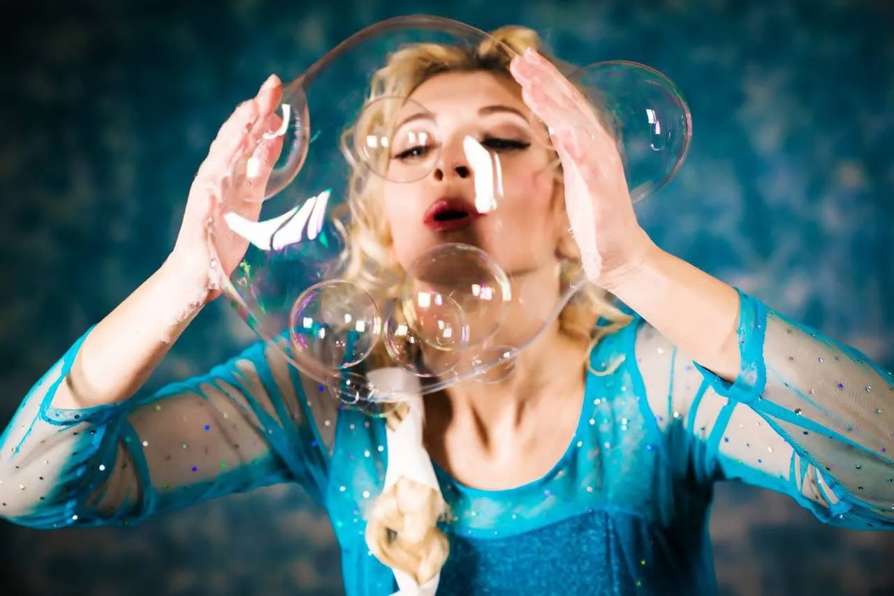 Artista in abito azzurro brillante che soffia bolle di sapone giganti durante lo spettacolo Bubble Show