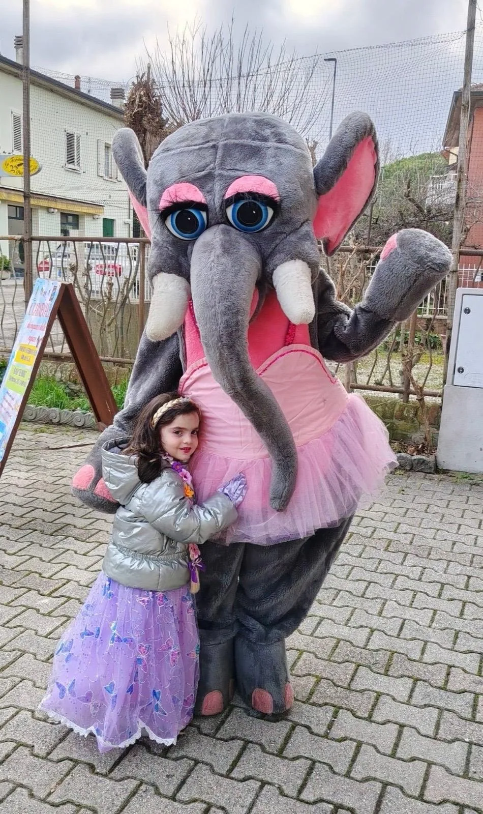 Bambina abbracciata alla mascotte dell'elefante con il tutù rosa