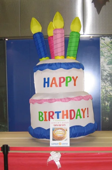 Torta gonfiabile a due piani con la scritta Happy Birthday e quattro candeline colorate