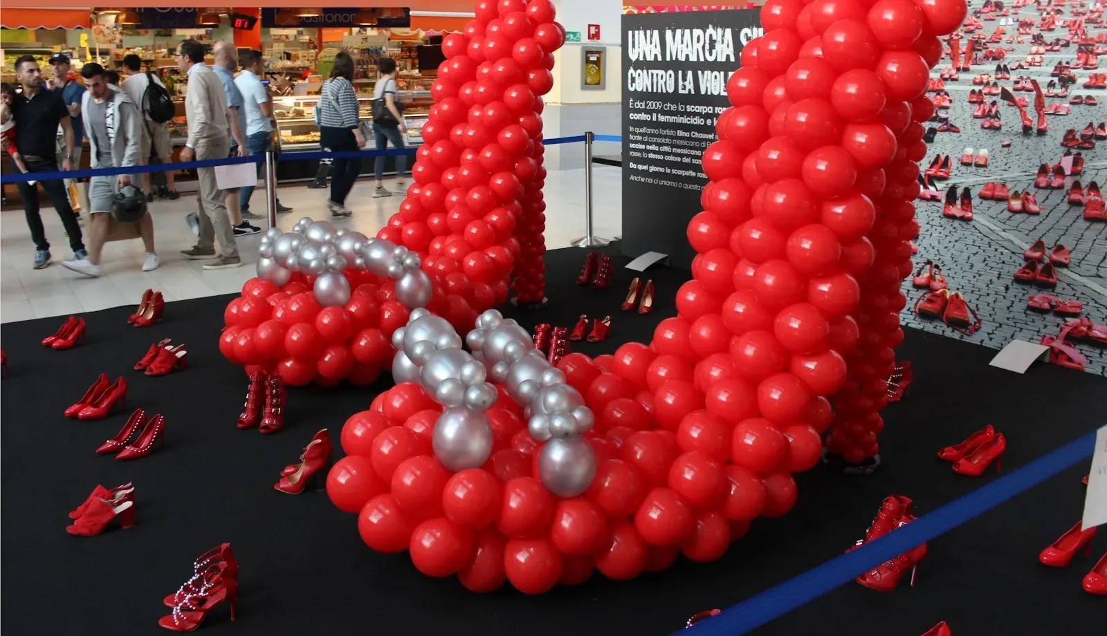 Scarpa rossa alta oltre due metri costruita con palloncini rossi e argento, allestita in una galleria commerciale