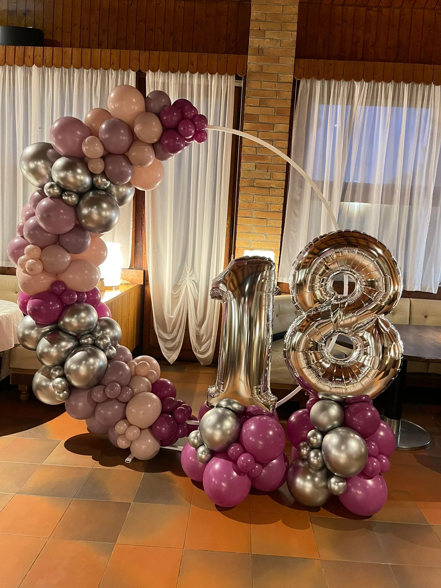 Arco circolare di palloncini rosa antico, prugna e argento cromato con numeri 18 giganti su colonne di palloncini fucsia