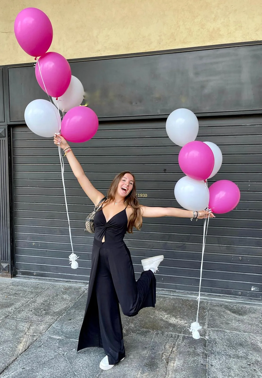 Ragazza in strada con due mazzi di palloncini a elio fucsia e bianchi, uno per mano