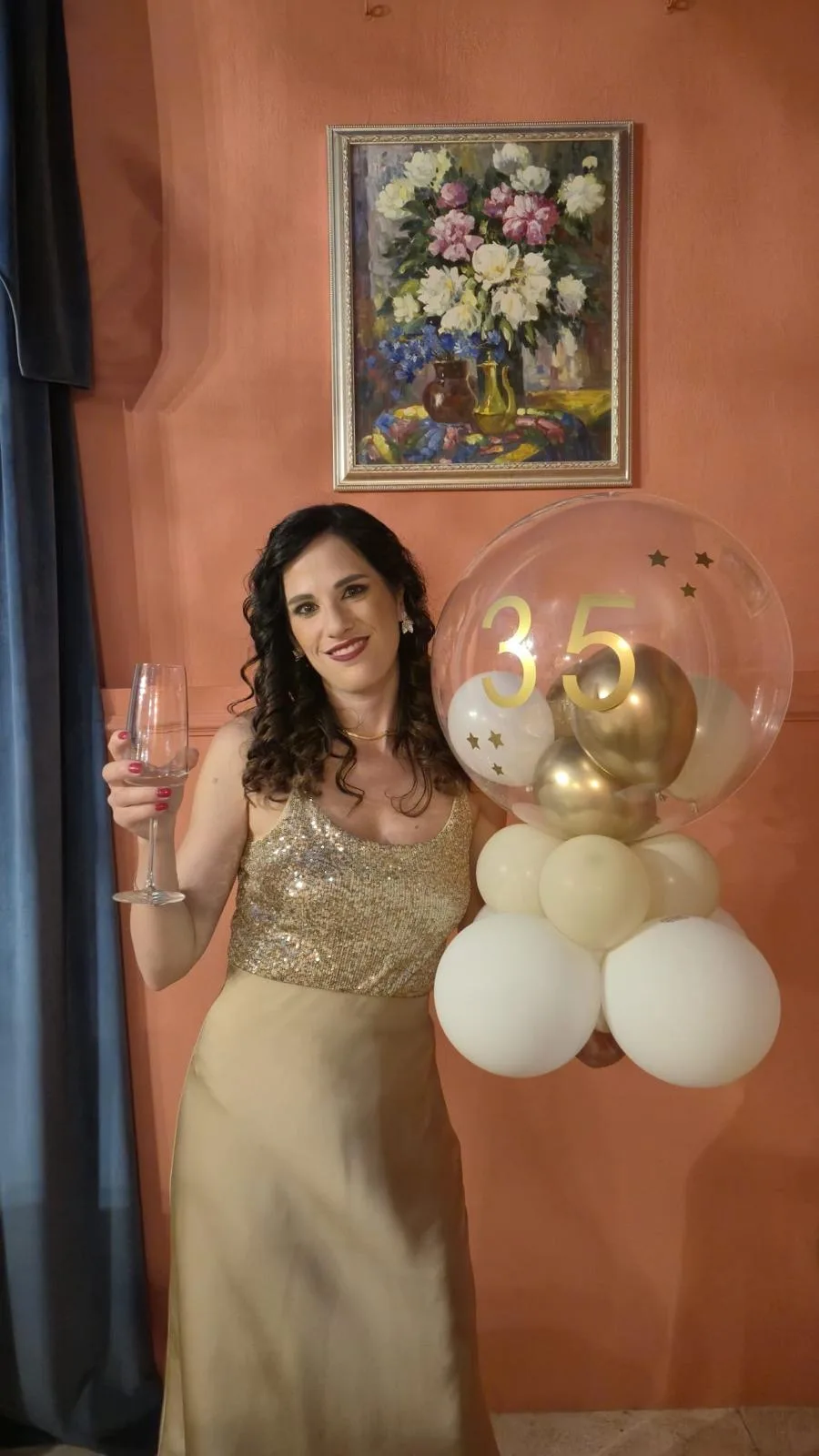 Donna con un calice in mano accanto a un palloncino bubble trasparente con il numero 35 in oro e base di palloncini avorio e oro