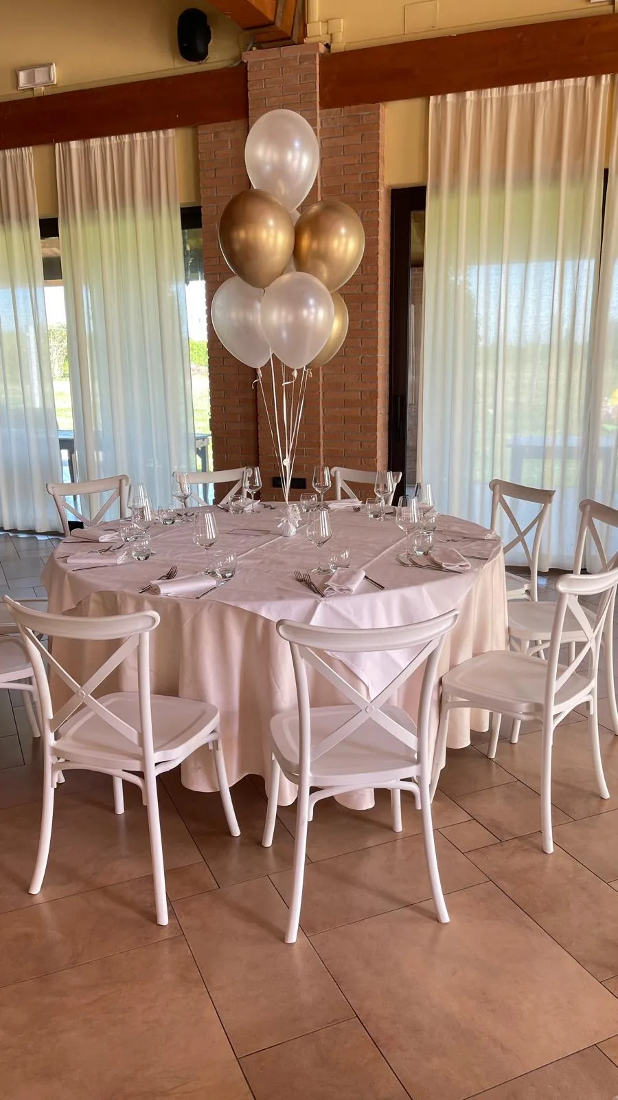 Tavolo rotondo apparecchiato in una sala ristorante con centrotavola di palloncini a elio bianchi, perlati e oro