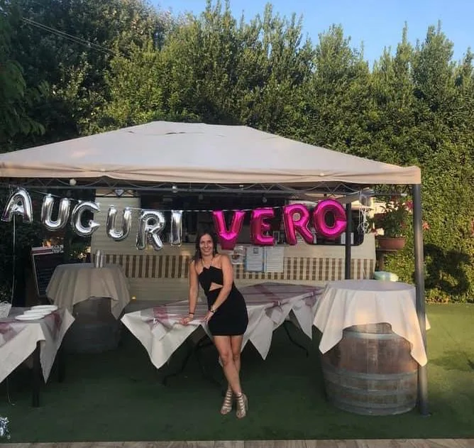 Scritta Auguri Vero composta con palloncini lettera argento e fucsia, appesa sotto il gazebo di un giardino apparecchiato