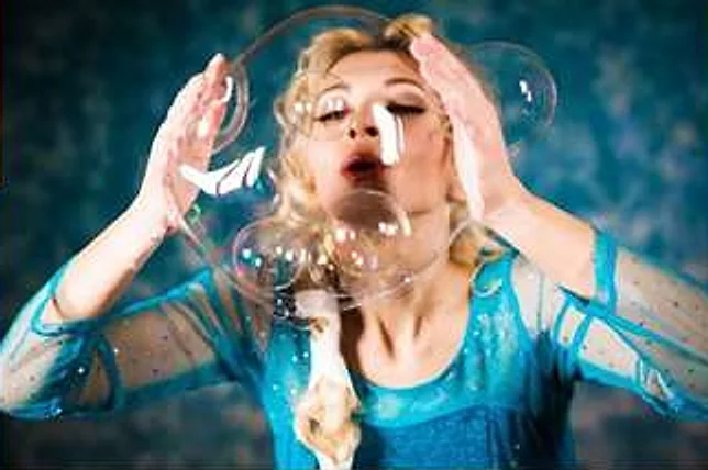 Artista in abito azzurro brillante che soffia bolle di sapone giganti durante lo spettacolo Bubble Show
